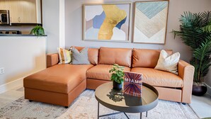 A modern living room with a sectional sofa, a coffee table, and two abstract paintings. - Coconut Grove Beauty! 1/1 Bayview Condo w/ Free Parking (Miami)