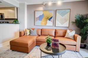 A modern living room with a sectional sofa, a coffee table, and two abstract paintings. - Coconut Grove Beauty! 1/1 Bayview Condo w/ Free Parking (Miami)
