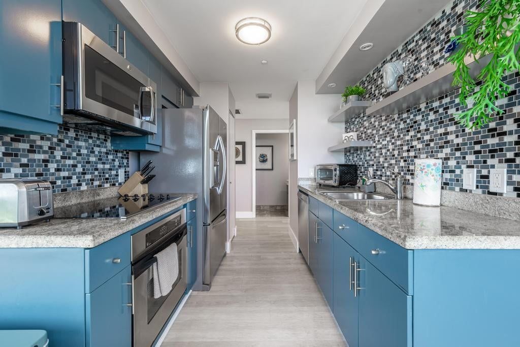 A modern kitchen with blue cabinets, stainless steel appliances, and a tiled backsplash.