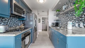 A modern kitchen with blue cabinets, stainless steel appliances, and a tiled backsplash.