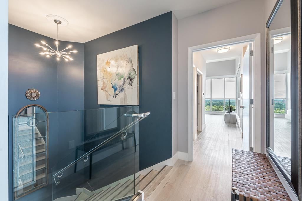 A modern interior with a staircase, a glass railing, a large abstract painting, and a view through a glass door.