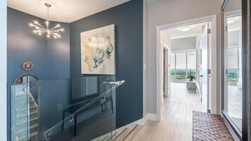 A modern interior with a staircase, a glass railing, a large abstract painting, and a view through a glass door.