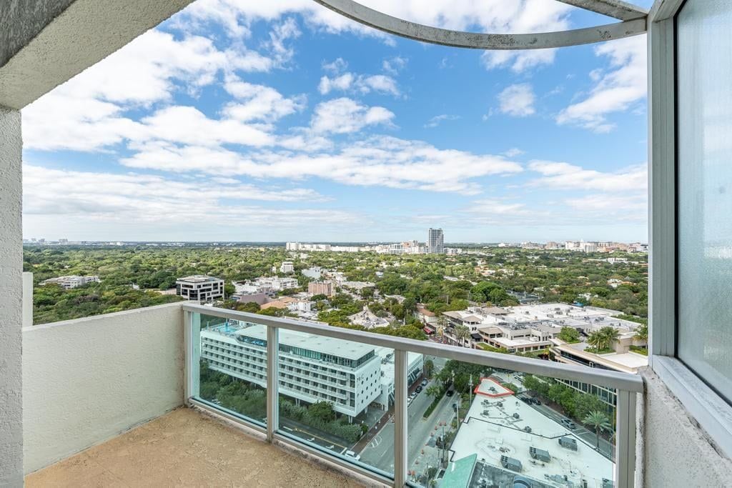 A balcony with a glass railing overlooking a cityscape with buildings and greenery.