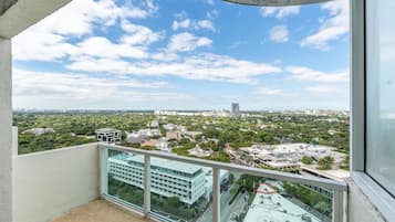 A balcony with a glass railing overlooking a cityscape with buildings and greenery.