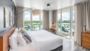 Ett modernt hotellrum med en stor säng, ett skrivbord och utsikt över stadsbilden genom stora fönster.