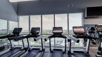 A gym with treadmills, a TV, and large windows overlooking a cityscape.