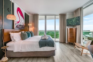 A hotel room with a large bed, a television, a balcony with a view, and a wooden floor. - Bright 1BR in Coconut Grove King Bed, Views, Pool & Parking (Miami)