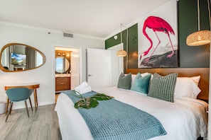 A hotel room with a bed, a desk, a mirror, a bathroom, and a painting of a flamingo. - Bright 1BR in Coconut Grove King Bed, Views, Pool & Parking (Miami)