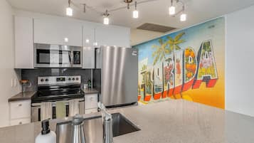 A modern kitchen with stainless steel appliances, a granite countertop, and a vibrant mural.