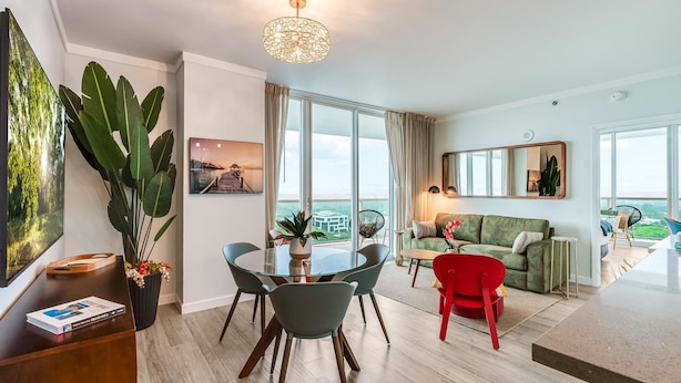 A modern living room with a dining area, large windows, and a view of the outdoors. - Bright 1BR in Coconut Grove King Bed, Views, Pool & Parking (Miami)
