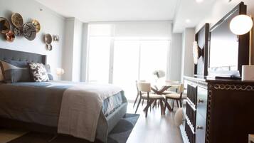 Un dormitorio moderno con una cama grande, un escritorio y una silla. Hay una ventana que ofrece luz natural y vistas al exterior.