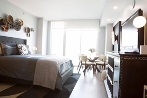 Un dormitorio moderno con una cama grande, un escritorio y una silla. Hay una ventana que ofrece luz natural y vistas al exterior.