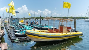 Een jachthaven met diverse boten aanmeren, een gele boot met 'Miami Watersports.com' op de zijkant, en enkele gele vlaggen.