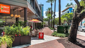 An outdoor seating area with tables and chairs, a sign for 'Carrot Express', and a 'Good Morning Coconut Grove' sign.