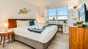 A hotel room with a bed, bedside table, desk, and a TV. - Modern 3br/3.5ba Grove Condo Views, Balconies, Full Kitchen + 3 Parking (Miami)