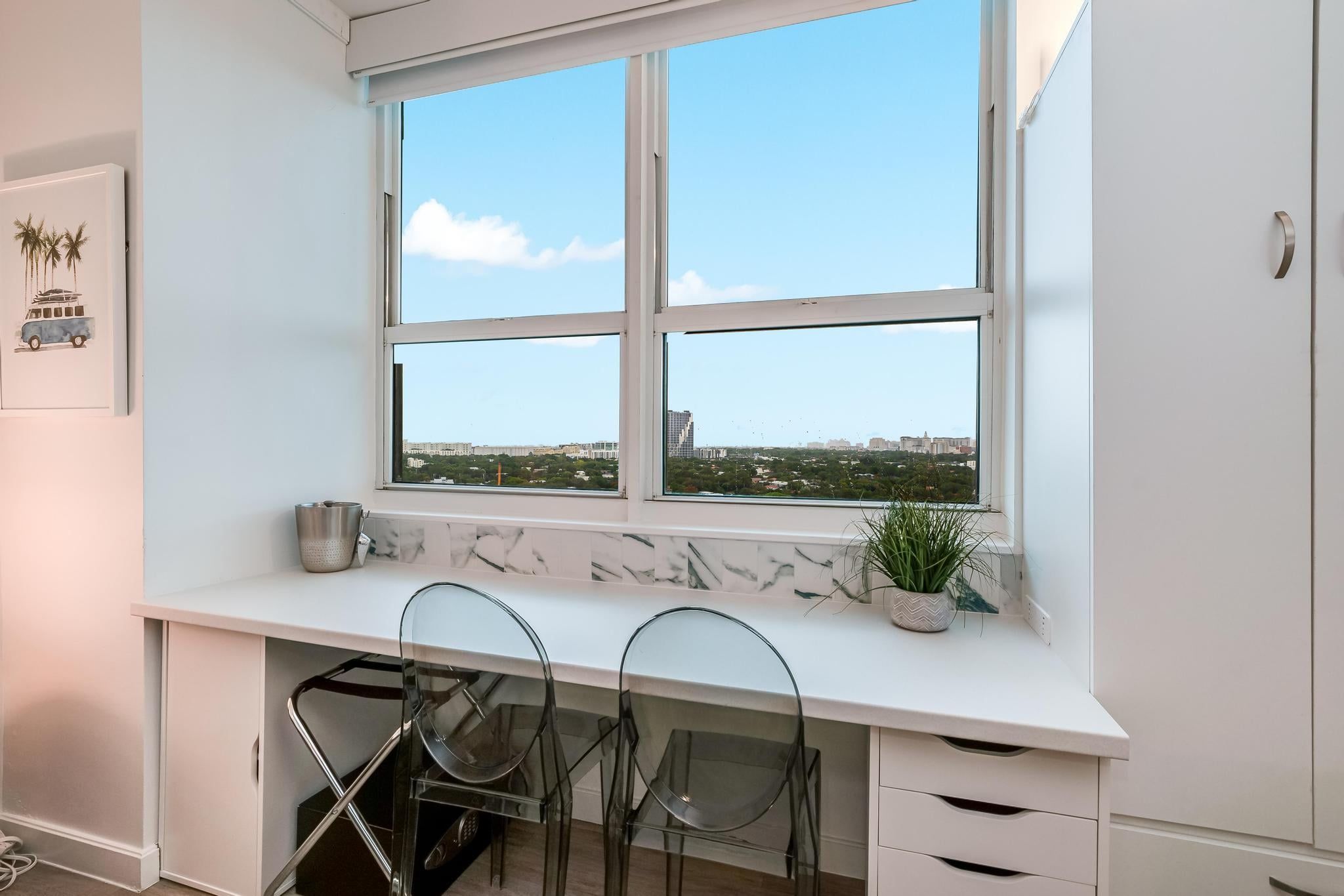 A kitchen with a large window, white cabinets, a marble backsplash, and a potted plant.