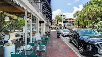 An outdoor cafe with tables and chairs, a street in the background, and parked cars.