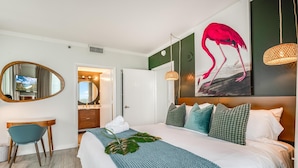 A hotel room with a bed, a desk, a mirror, a bathroom, and a painting of a flamingo. - Modern 3br/3.5ba Grove Condo Views, Balconies, Full Kitchen + 3 Parking (Miami)