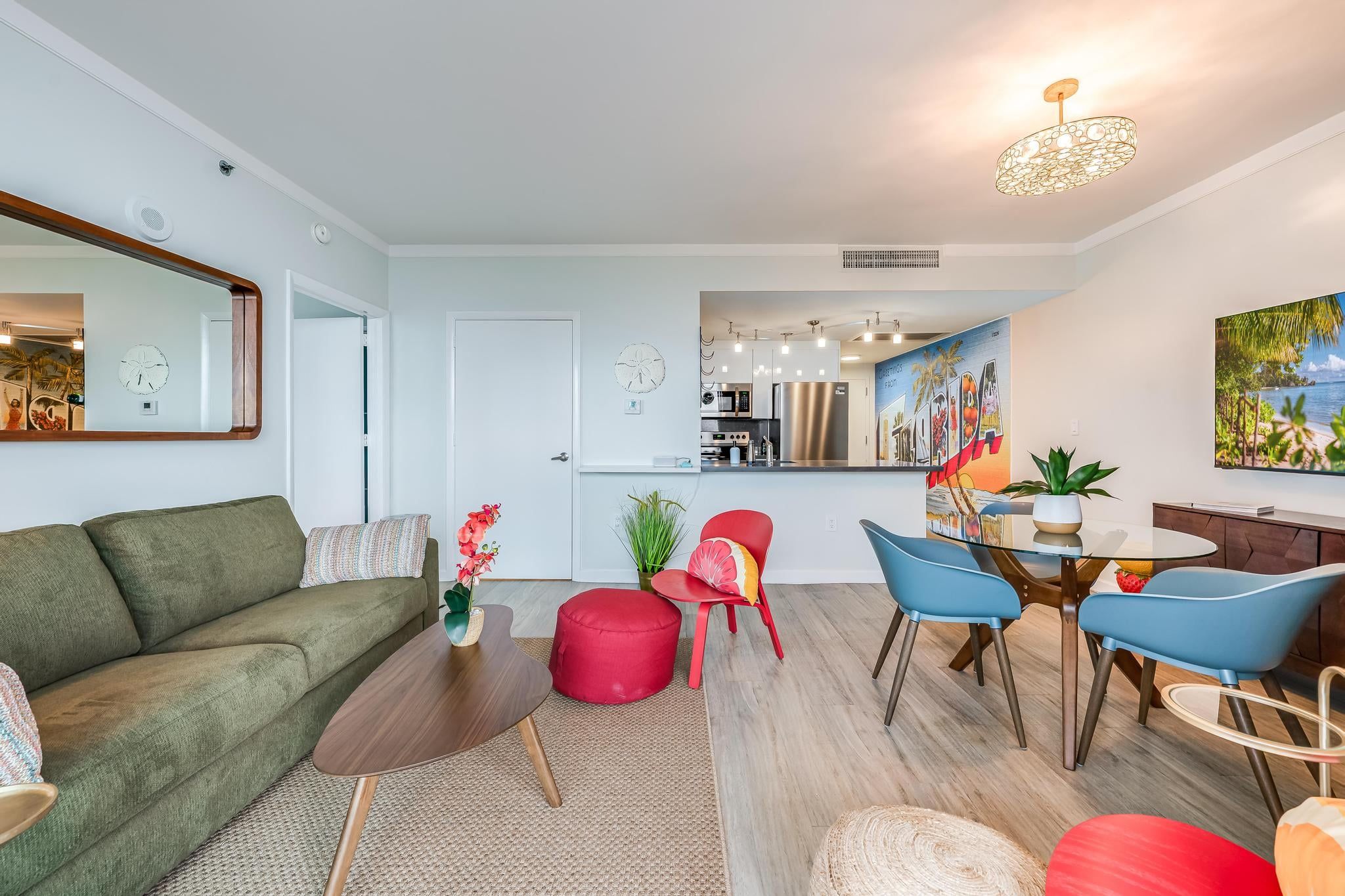 A modern living room with a sofa, red ottoman, and a dining area with chairs and a table.
