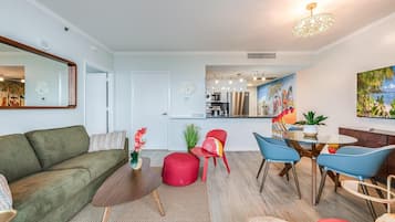 A modern living room with a sofa, red ottoman, and a dining area with chairs and a table.