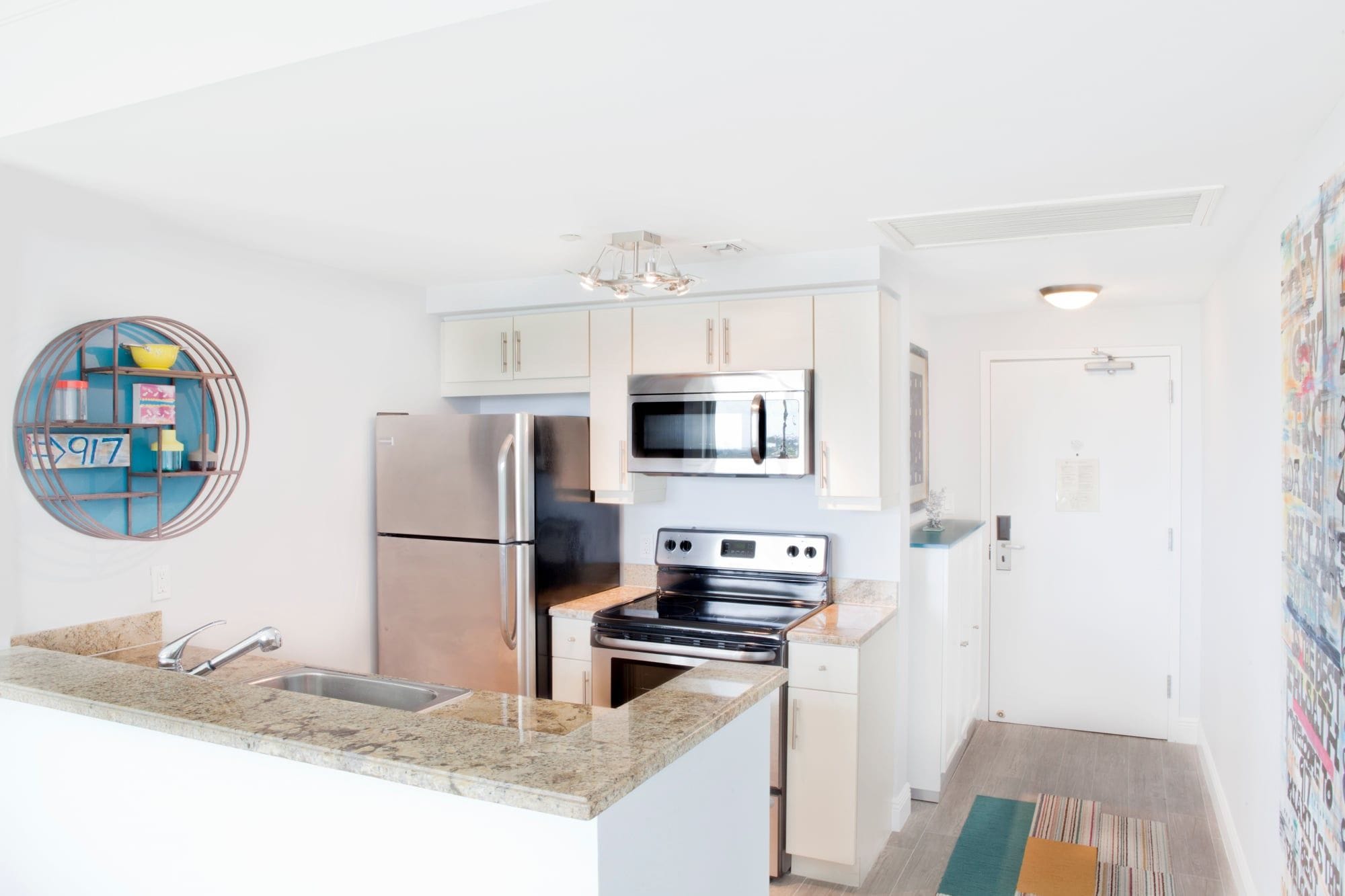 A modern kitchen with stainless steel appliances, a granite countertop, and a decorative wall piece.