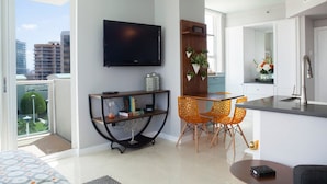 A modern living room with a flat-screen TV, a dining area with orange chairs, and a kitchen with white cabinets. - Coconut Grove:10th Fl Studio-parking Included (Miami)