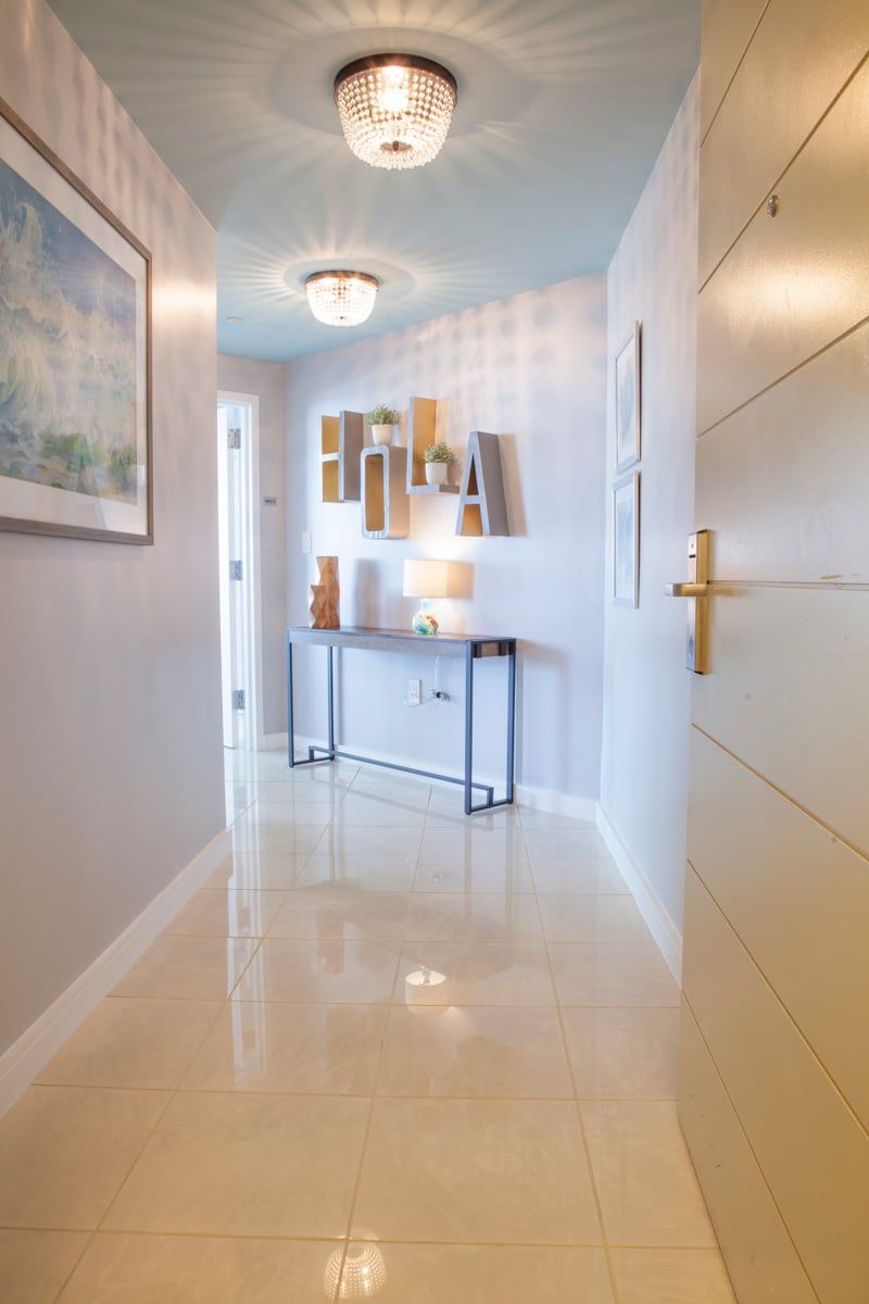 A hallway with a polished floor, a console table with a lamp, and a door with a gold handle.