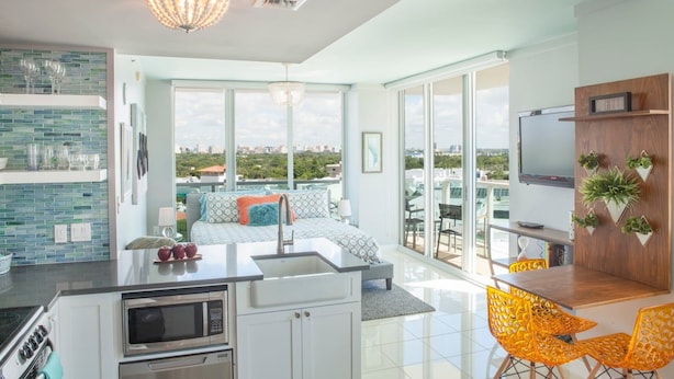 A modern kitchen with a built-in microwave, a dining area with yellow chairs, and a large window offering a city view. - Coconut Grove:10th Fl Studio-parking Included (Miami)