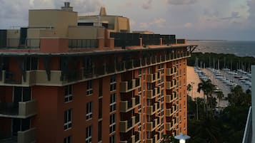 Un immeuble à plusieurs étages doté de balcons, une marina avec des bateaux, et un coucher de soleil en arrière-plan.