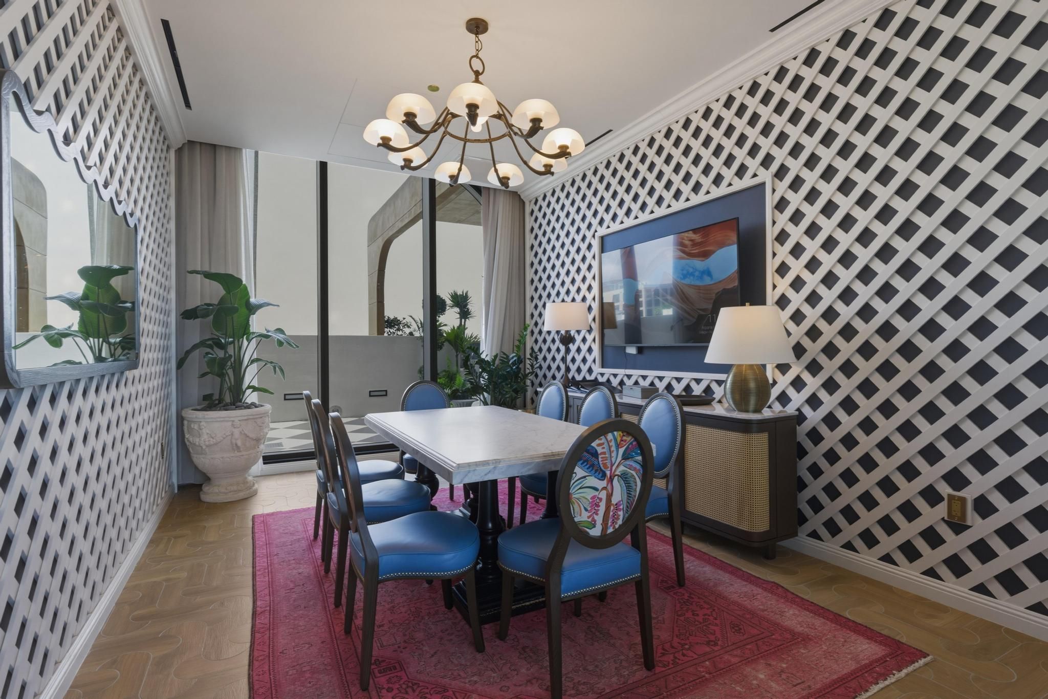 A dining area with a table, chairs, a chandelier, a TV, and a patterned wall.