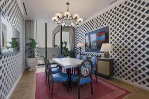 A dining area with a table, chairs, a chandelier, a TV, and a patterned wall. - Walk to Wynwood Walls 1BR + Den 2 Baths (Miami)