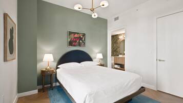 Une chambre à coucher comprenant un lit, deux tables de chevet, une commode, une œuvre d’art accrochée au mur et une porte.