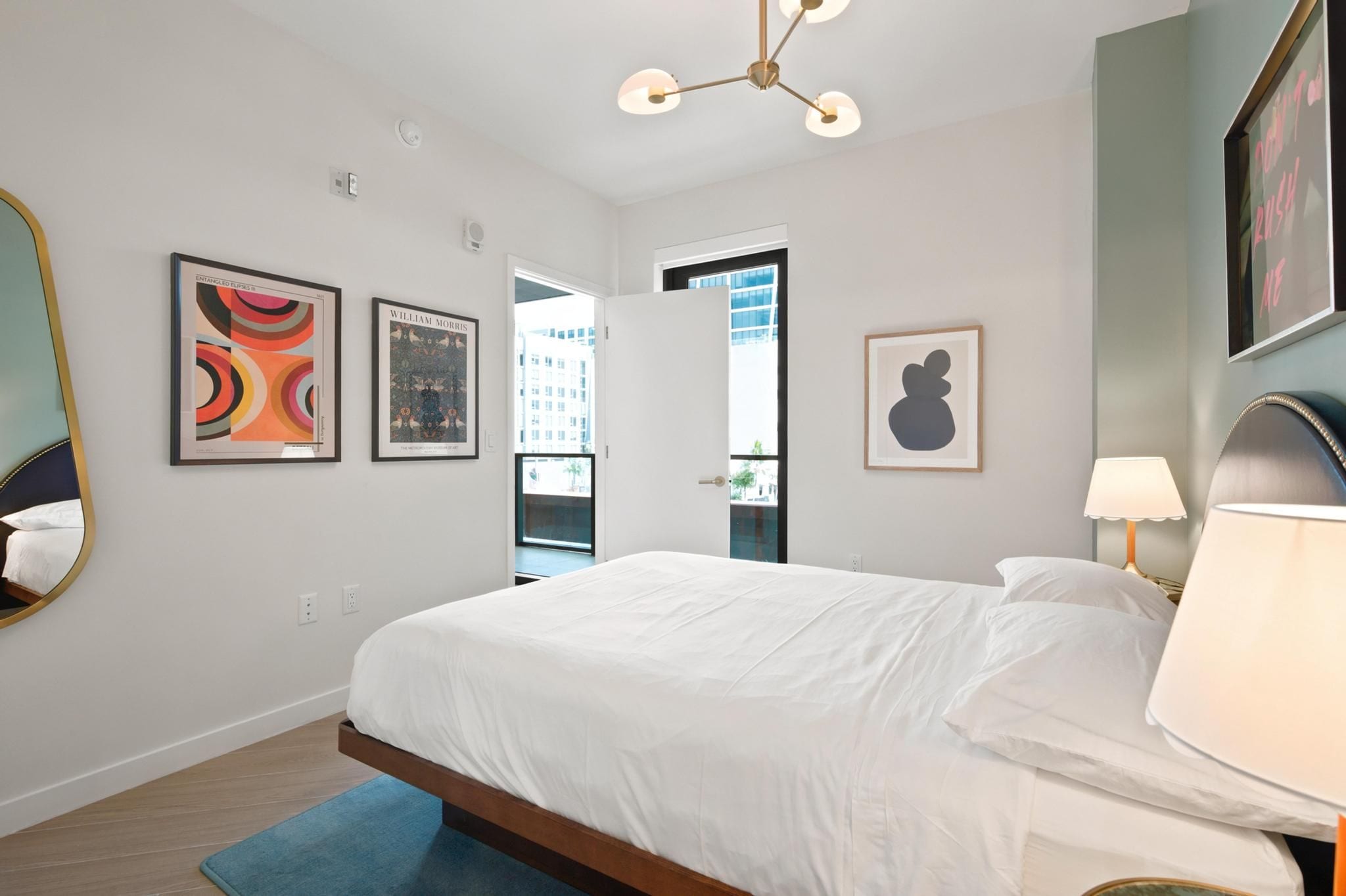 Una habitación de hotel moderna con una cama grande, un tapete azul, un espejo y cuadros en las paredes.