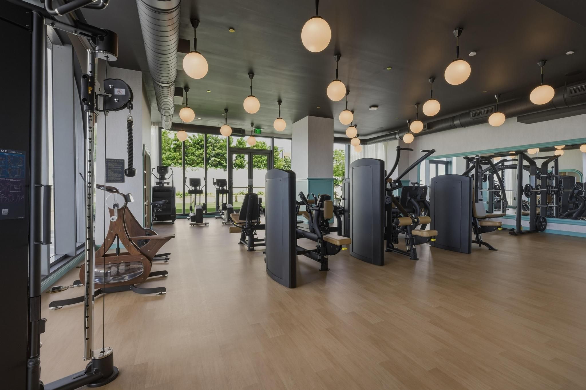 Un gimnasio con equipo de ejercicio, piso de madera e iluminación colgante.