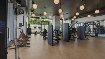 Un gimnasio con equipo de ejercicio, piso de madera e iluminación colgante.