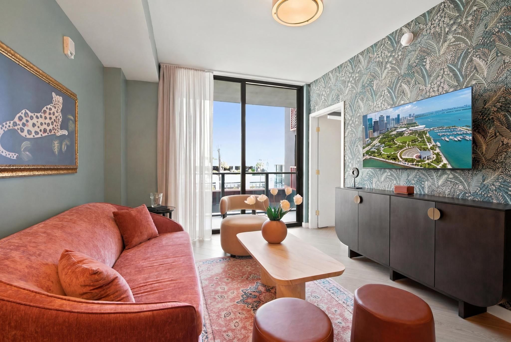 Uma sala de estar moderna com sofá, mesa de centro e apoio para os pés, uma área de jantar com mesa e uma grande janela com vista para a paisagem urbana.