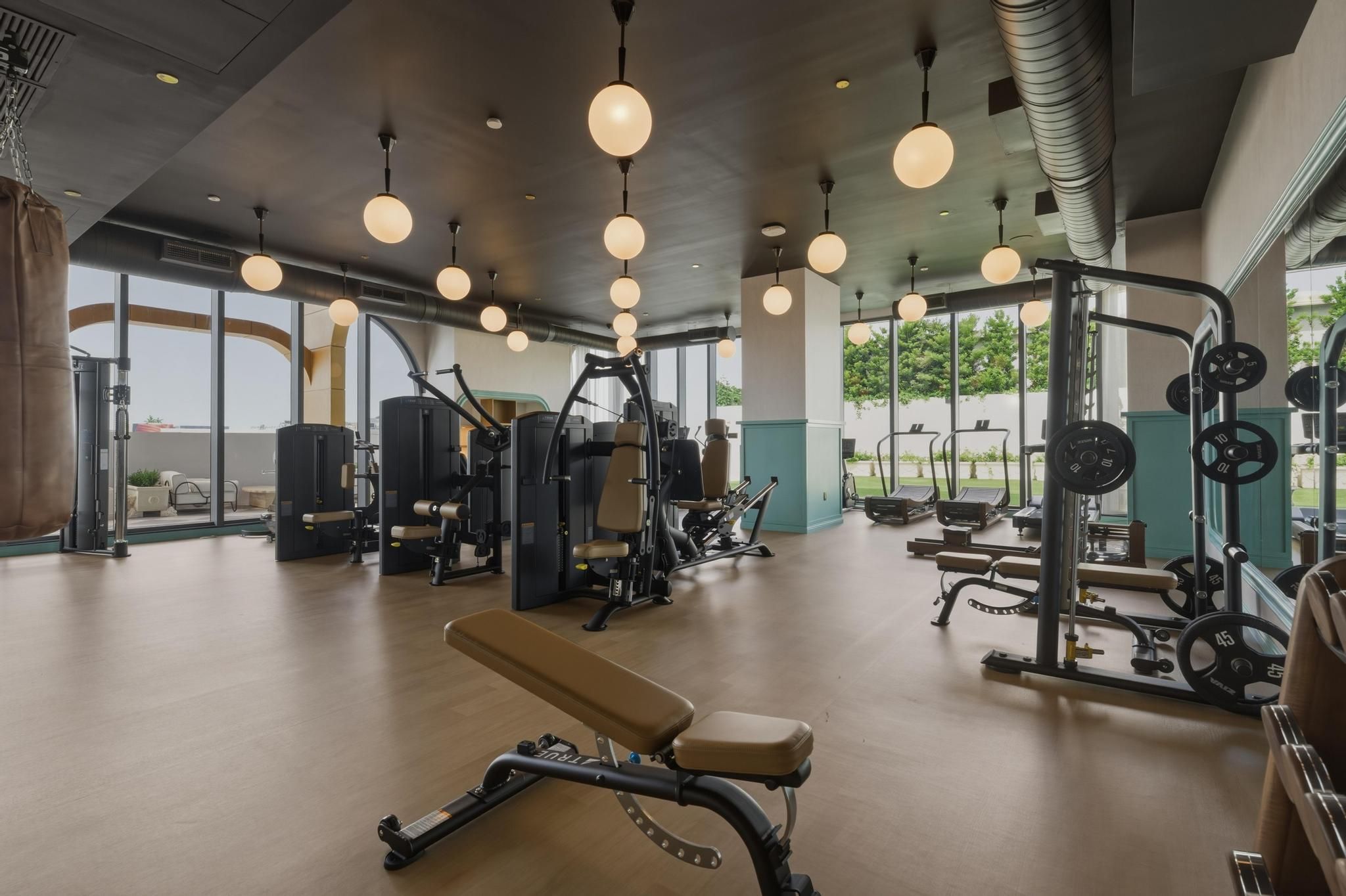 A gym with exercise equipment, large windows, and hanging lights.