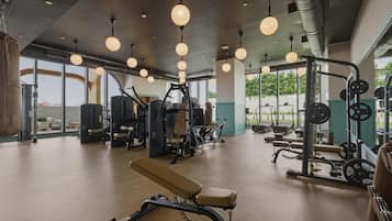 Uma academia com equipamentos de ginástica, janelas amplas e luminárias pendentes.