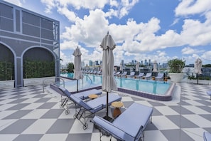 A rooftop pool with lounge chairs and umbrellas, a checkered floor, and a city skyline in the background. - Luxury Wynwood 2BR Pool, Gym, Walk to Restaurants & Art (Miami)