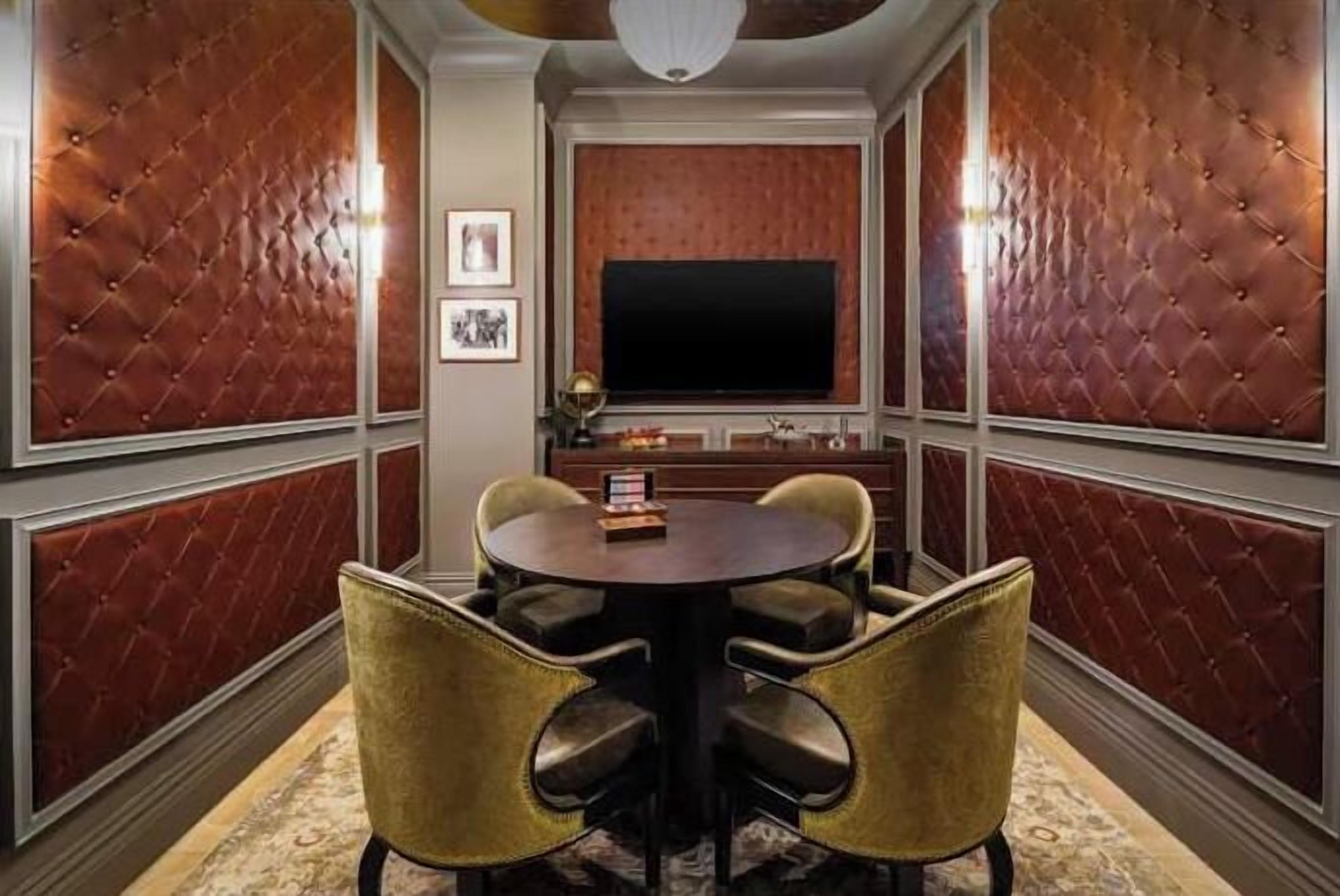 A room with a round table, four chairs, a flat-screen TV, and a wall with a patterned design.