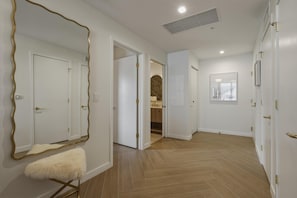 A hallway with white doors, a large mirror with a gold frame, and a white furry bench. - Luxury Wynwood 2BR Pool, Gym, Walk to Restaurants & Art (Miami)