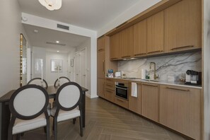 A modern kitchen with wooden cabinets, a marble countertop, and a dining area with a table and chairs. - Luxury Wynwood 2BR Pool, Gym, Walk to Restaurants & Art (Miami)