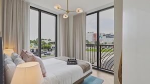 Et hotelværelse med en stor seng, udsigt over byen gennem gulv til loft-vinduer, en balkon med gelænder og en moderne lysekrone.