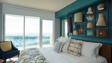 Un dormitorio con una cama grande, vistas al mar a través de ventanales del suelo al techo y una lámpara fijada a la pared.