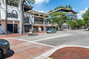 A street view with a modern building, a golf cart, and a pedestrian crossing. - Cozy Grove Stay Free Parking, Pool Access, Walk to Cafés & Parks (Miami)