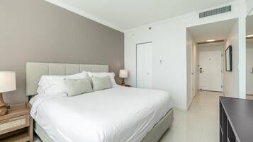 Un dormitorio con una cama, mesitas de noche, un aparador y una puerta que da a otra habitación.