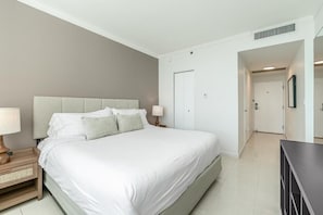 Un dormitorio con una cama, mesitas de noche, un aparador y una puerta que da a otra habitación.