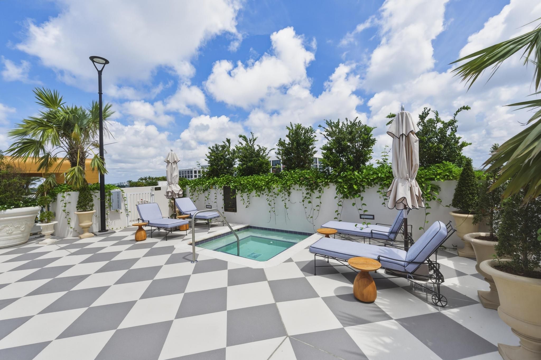 A rooftop pool area with checkered flooring, lounge chairs, and umbrellas.