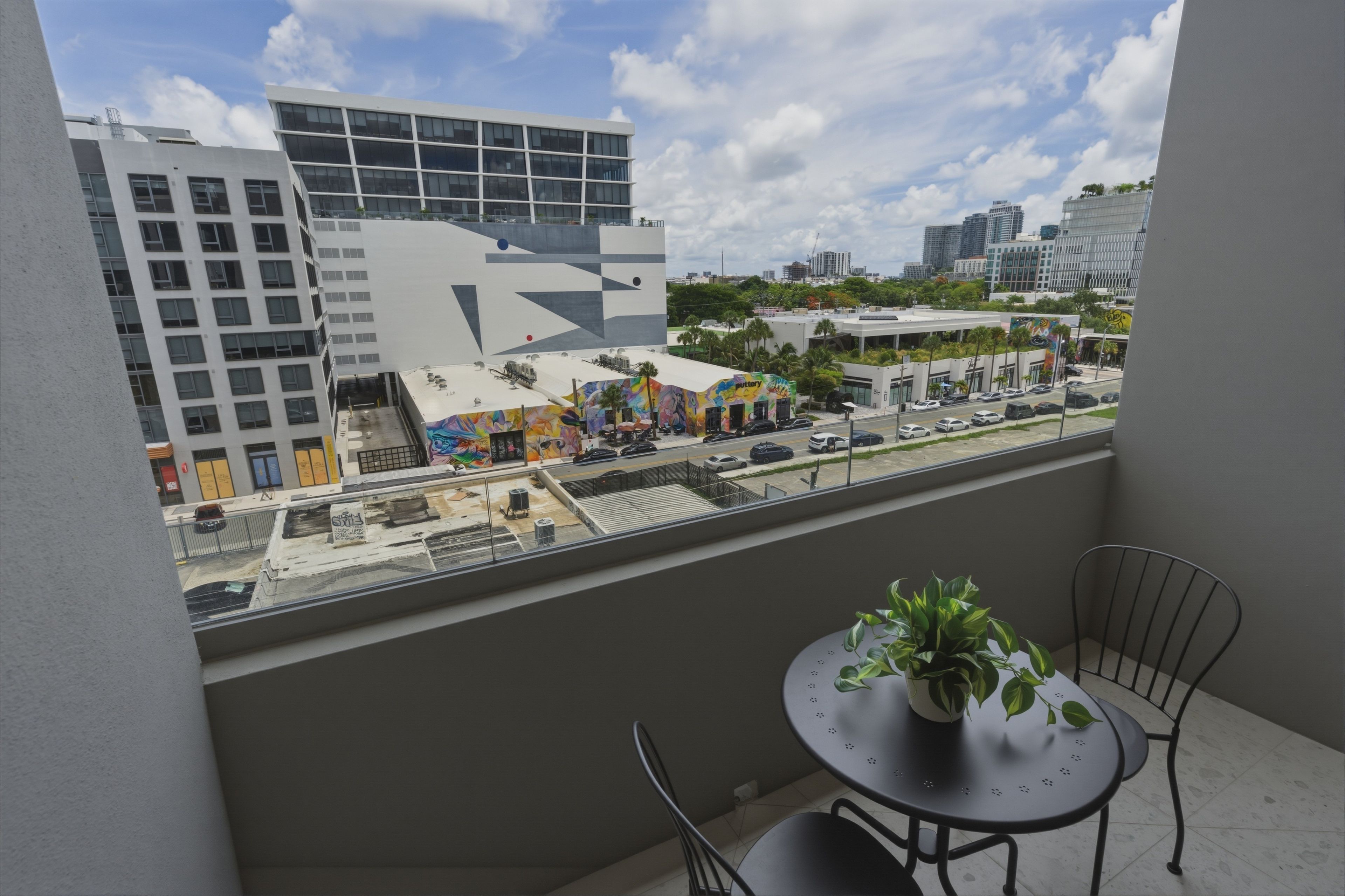 Uma varanda com vista para um horizonte urbano, incluindo edifícios modernos e uma rua com carros estacionados.