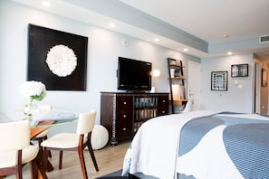 A modern hotel room with a large bed, a flat-screen TV, a dining area with a glass table, and a bookshelf. - Deluxe Studio in Coconut Grove-city & Bay Views...includes Parking (Miami)